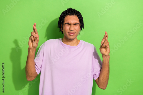 Photo of nervous young person closed eyes crossed fingers hope expectation isolated on green color background