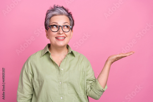 Photo of business lady grandmother khaki stylish shirt holding arm empty space proposition advertisement isolated on pink color background
