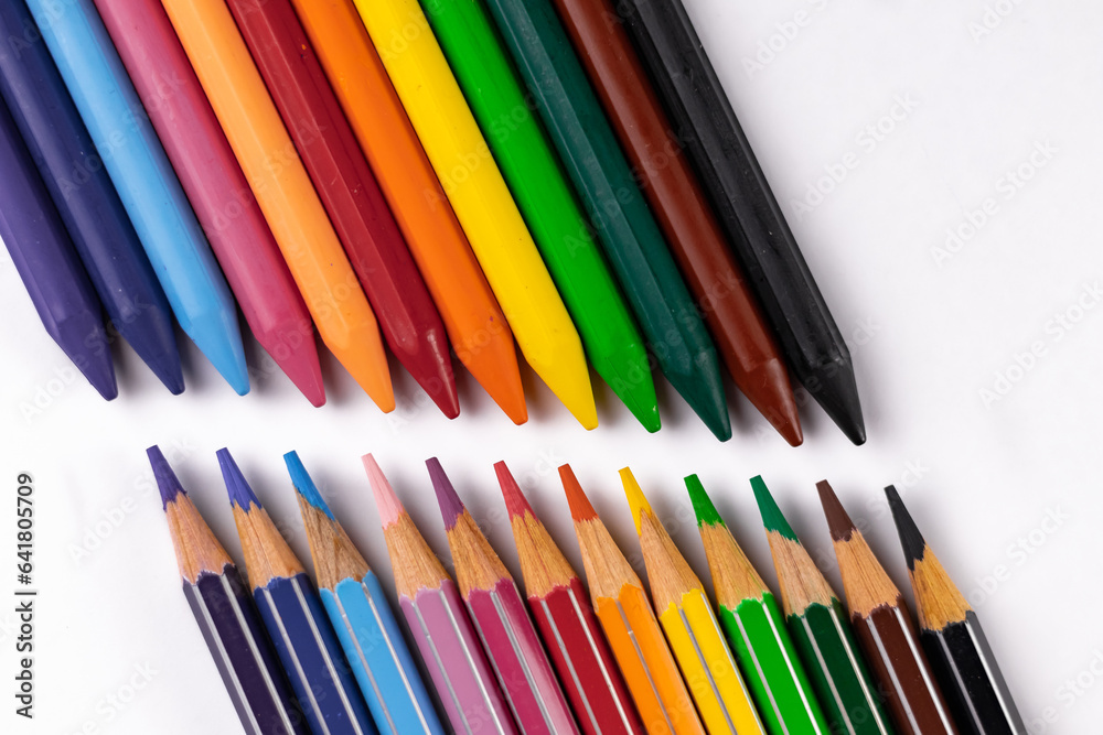 High angle close up shot of crayons and pencil colors pointing towards each other placed on white background. High angle close up shot of crayons and pencil colors pointing towards each other placed on white background.