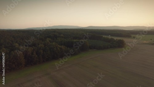 Dramatic and epic drone shot of the woods and fields  with mountains in the background bird view, during a sunset or a sunrise dusk or dawn