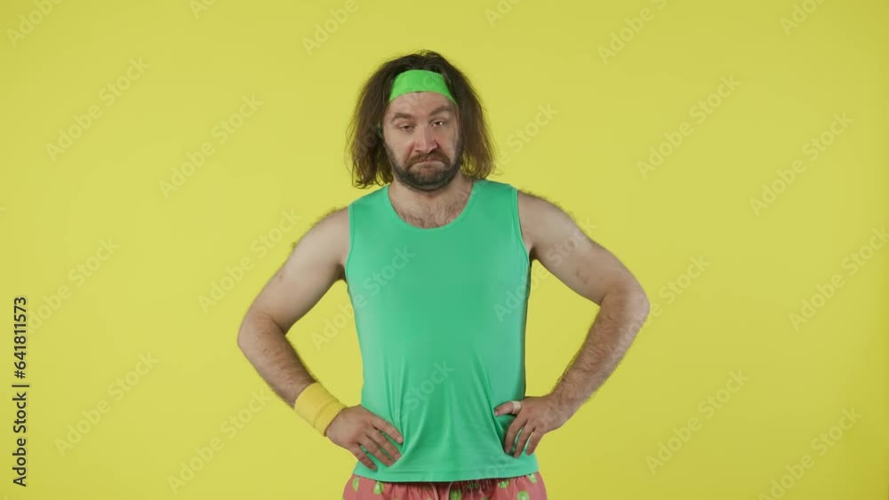 Man in green top and headband came to gym, looks confused and shocked at people around. Isolated on yellow background. Man in green top and headband came to gym, looks confused and shocked at people around. Isolated on yellow background.