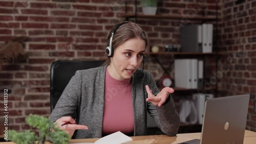 Close up portrait young woman in headphones holding online video call meeting with tutor on laptop, discussing educational material, making notes, foreign language distant study e-learning concept.