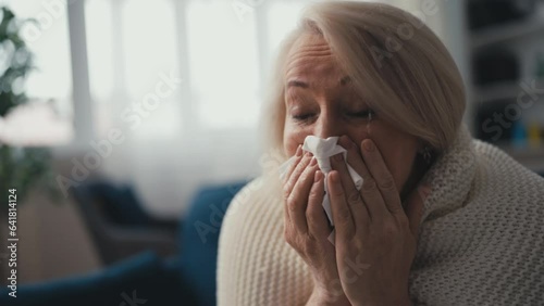 Woman in her 50s suffering from fever and runny nose, sneezing on the couch photo
