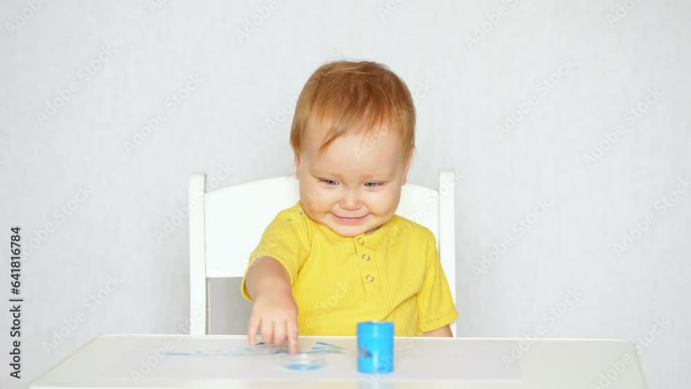 Positive toddler girl plays with sticky slime from blue jar sitting at table in light studio. Concept of children joy and entertainment Positive toddler girl plays with sticky slime from blue jar sitting at table in light studio. Concept of children joy and entertainment