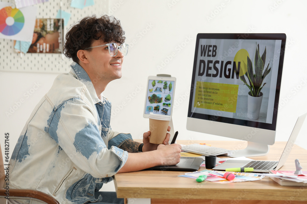 Male graphic designer with cup of coffee working at table in office