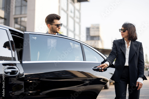 Female chauffeur helps a business man to get out of the car. opening a door. Concept of personal driver, luxury taxi or business trips - Stock Image - Everypixel