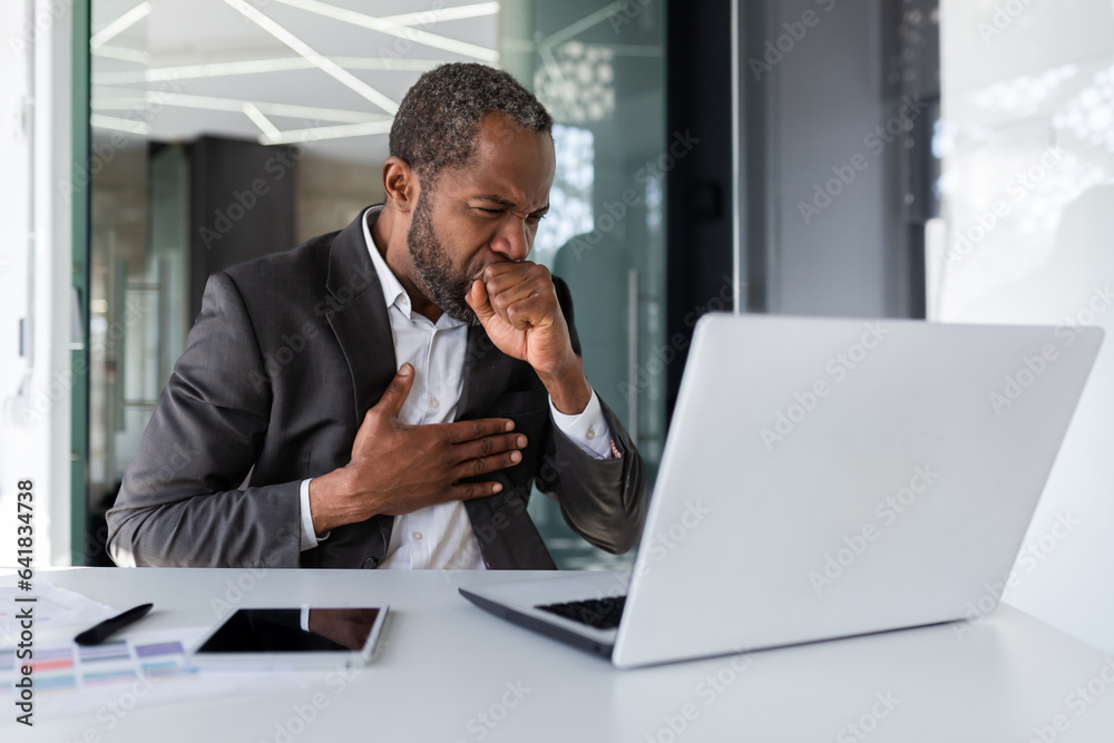 Sick senior mature african american boss coughing at workplace inside office, businessman working with laptop sitting at desk. Sick senior mature african american boss coughing at workplace inside office, businessman working with laptop sitting at desk.