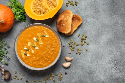 Pumpkin cream soup with toasts on a gray concrete background. Cozy thanksgiving dinner. Top view, flat lay.