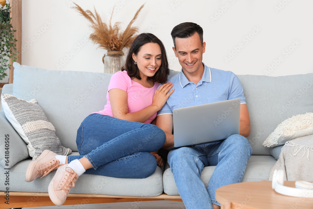 Happy couple using laptop while sitting on sofa in living room at home Happy couple using laptop while sitting on sofa in living room at home