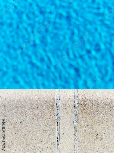 Close-up of the white pool edge contrasting with the light blue water in the pool. The edge is in focus, the water is blurred.