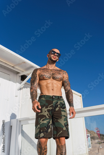 Chico joven tatuado y musculoso posando en verano en playa soleada © MiguelAngelJunquera