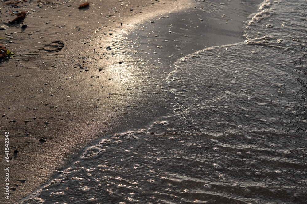 Soft ocean wave on sandy beach on sunset time, selective focus, textured pattern Soft ocean wave on sandy beach on sunset time, selective focus, textured pattern