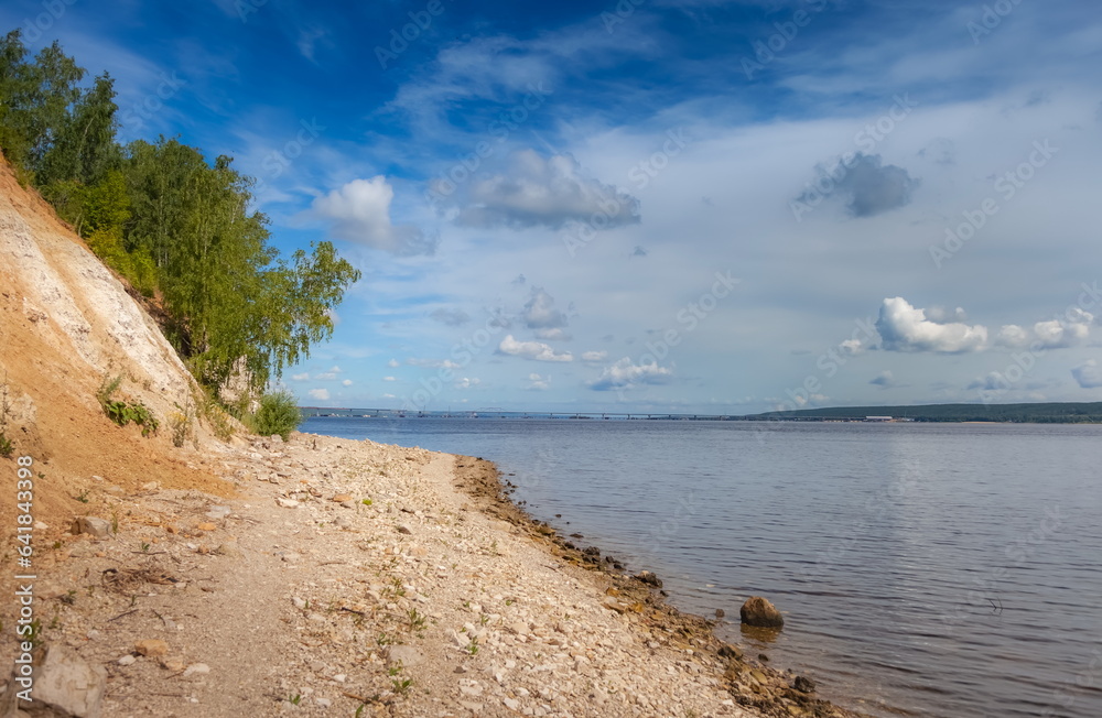 The bank of a large river with trees on the background of a blue sky with clouds in summer The bank of a large river with trees on the background of a blue sky with clouds in summer