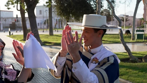 adult male dressed as a huaso clapping with his cueca dance partner in the square photo