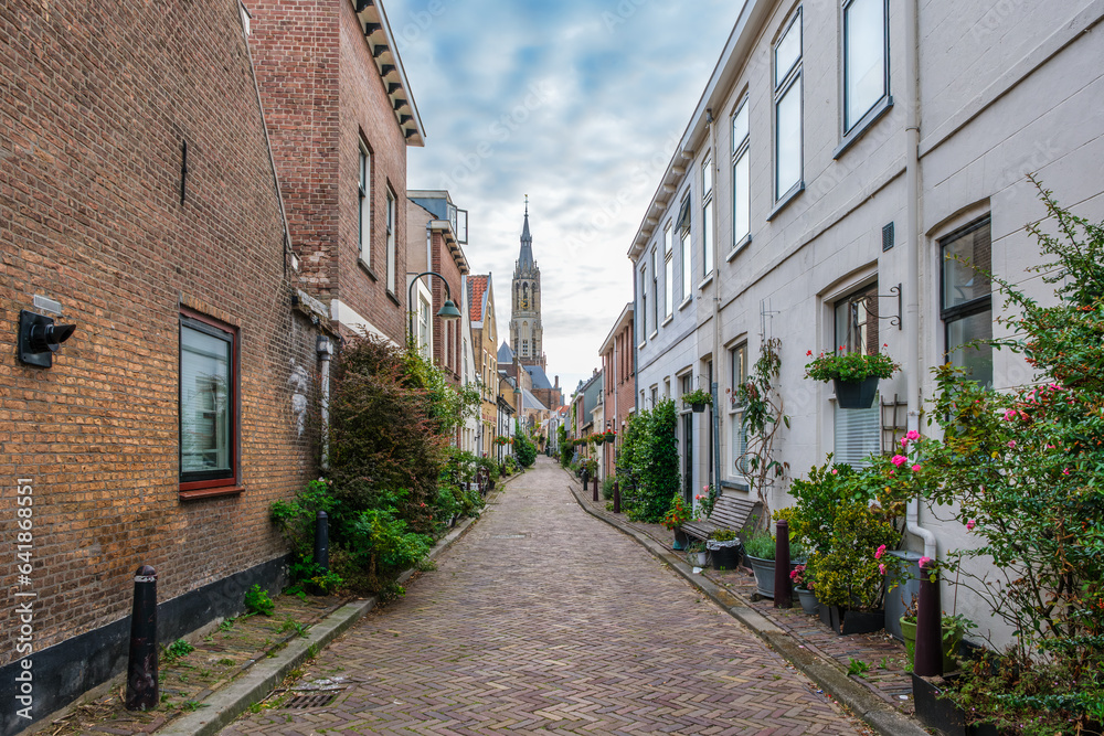 Picturesque Delft cityscape with a view through a narrow ancient alley on the tower of the famous Nieuwe Kerk. Delft, the Netherlands. Old alley called The Trompet Straat