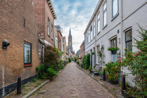 Picturesque Delft cityscape with a view through a narrow ancient alley on the tower of the famous Nieuwe Kerk. Delft, the Netherlands. Old alley called The Trompet Straat photo