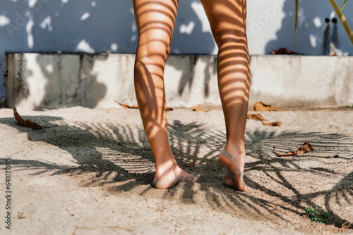 Una joven mujer descalza en la arena con sombra de palmera en su piel photo