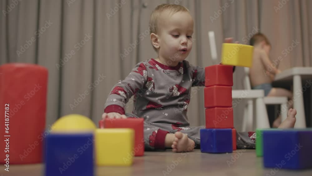 baby toddler sits on floor in living room plays multi-colored plastic cubes builds tower building breaks. little child development coordination, motor skills training education. leisure games home kid baby toddler sits on floor in living room plays multi-colored plastic cubes builds tower building breaks. little child development coordination, motor skills training education. leisure games home kid