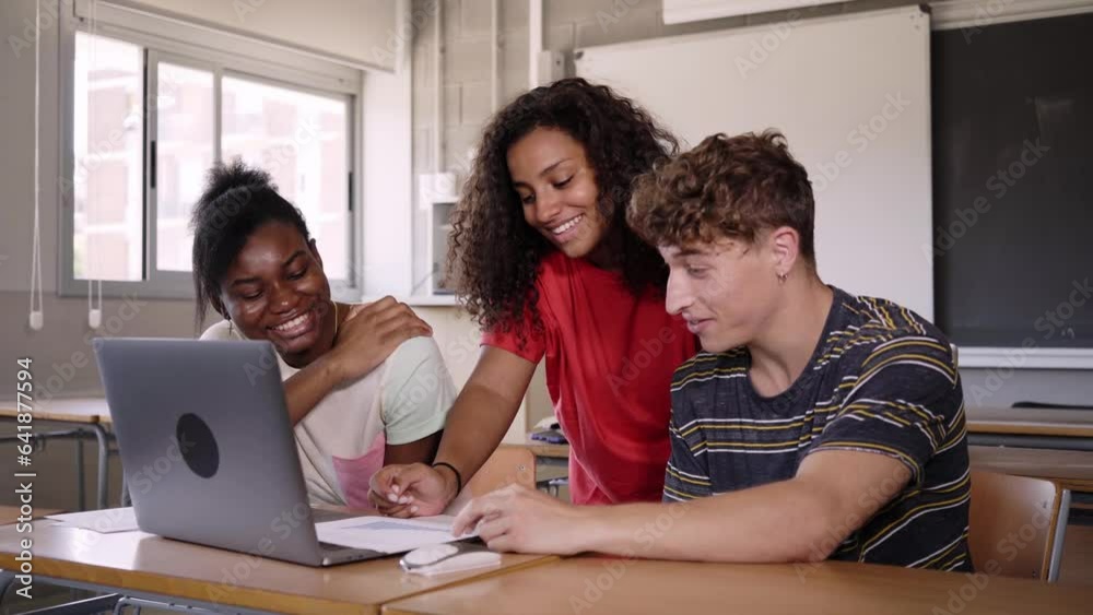 Group of cheerful young multiracial students using laptop computer talking about final year project in university classroom. Education concept. Generation Z people and final exams. Group of cheerful young multiracial students using laptop computer talking about final year project in university classroom. Education concept. Generation Z people and final exams.