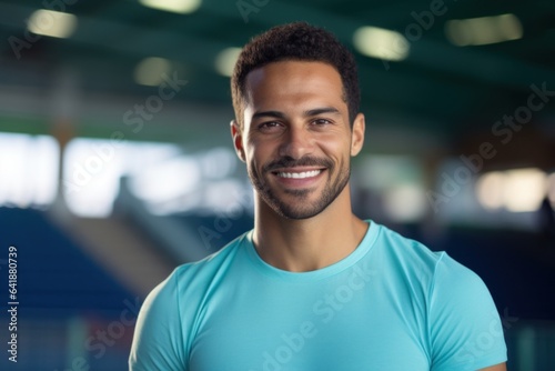 An athlete of Middle Eastern descent wearing a Polo in a bright turquoise hue standing still against a hazy sports arena background.