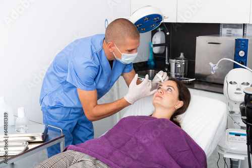 Skilled male cosmetologist filling females wrinkles using rejuvenating injections in clinic of aesthetic medicine