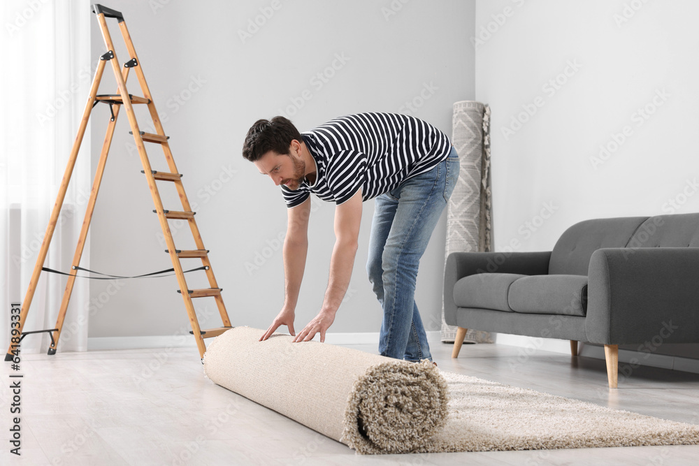 Man unrolling new clean carpet in room