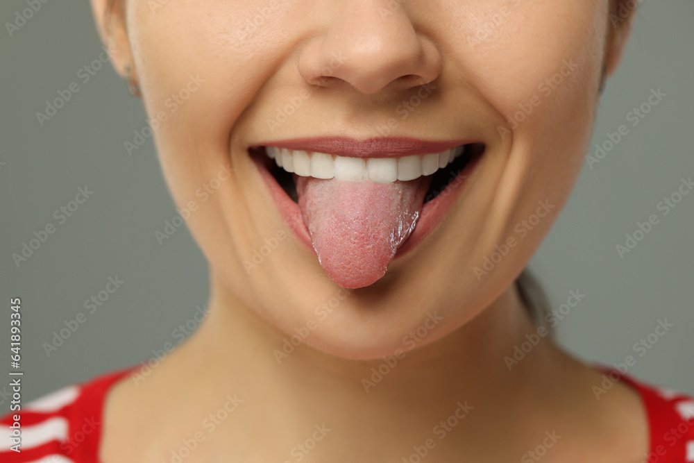 Happy young woman showing her tongue on grey background, closeup Happy young woman showing her tongue on grey background, closeup