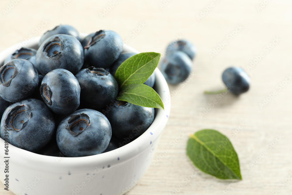 Bowl of fresh tasty blueberries with leaves on table, closeup. Space for text Bowl of fresh tasty blueberries with leaves on table, closeup. Space for text