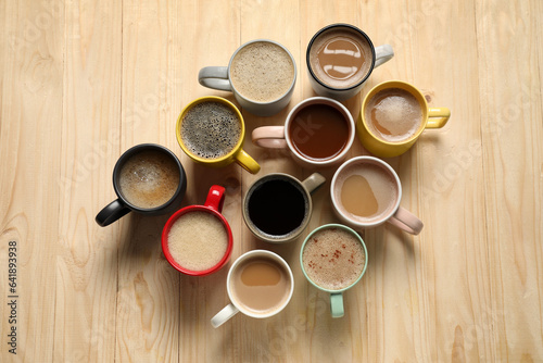 Many cups with different aromatic coffee on wooden table, flat lay