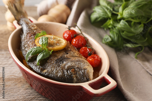 Tableau sur toile Delicious roasted dorado fish with tomatoes, basil and lemon on wooden table, cl