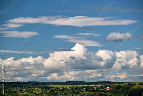 Bright landscape of white puffy cumulus clouds on blue clear sky over rural area