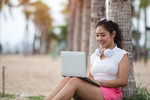 Happy woman typing on laptop computer sitting on the tropical sandy beach