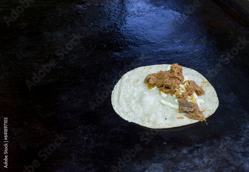 Tortilla de harina cocida con carne de res deshebrada y queso blanco en un comal caliente, comida mexicana.