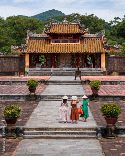 Hue, Vietnam, Hien Duc Gate At Mausoleum Of Minh Mang. . Against the background of the mausoleum, three girls in traditional Vietnamese costumes are standing with their backs.
