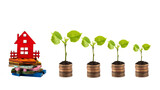 Young sprouts with green leaves on columns of coins and miniature wooden houses on a white background