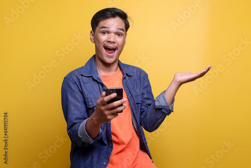 Happy excited Asian man showing surprise expression with open arms while holding smartphone © Queenmoonlite Studio