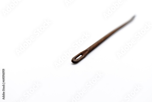 This mattress thread needle made of metal looks rusty and was photographed on the isolated white background