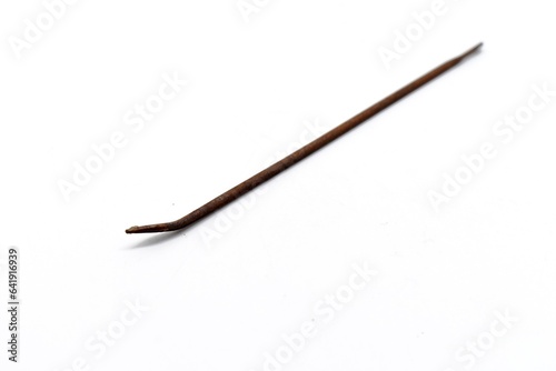 This mattress thread needle made of metal looks rusty and was photographed on the isolated white background