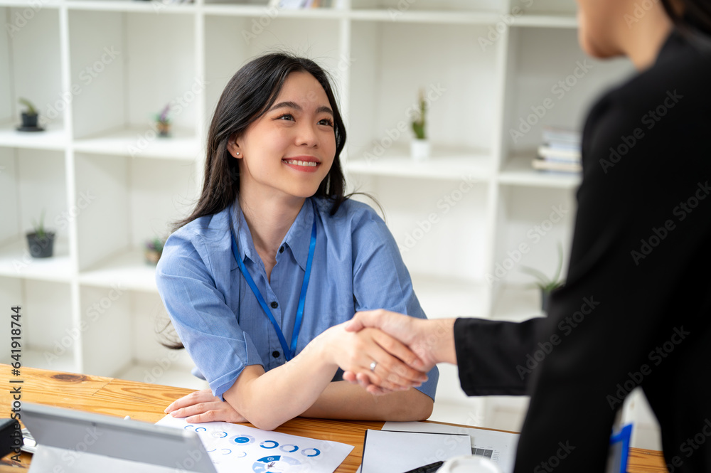 Fototapeta premium A beautiful Asian businesswoman is shaking hands with her colleague, making a deal