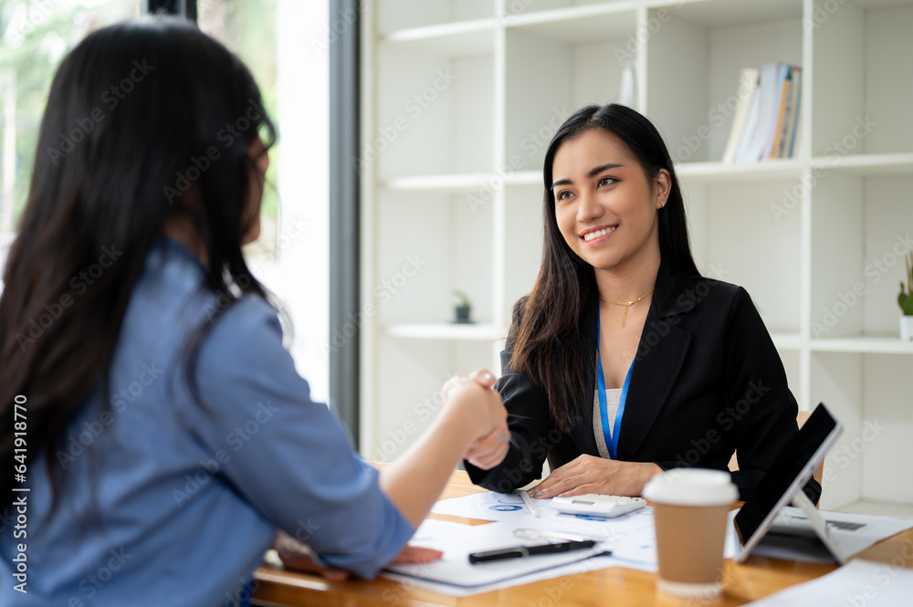 A gorgeous Asian businesswoman is shaking hands with a female client in the office A gorgeous Asian businesswoman is shaking hands with a female client in the office