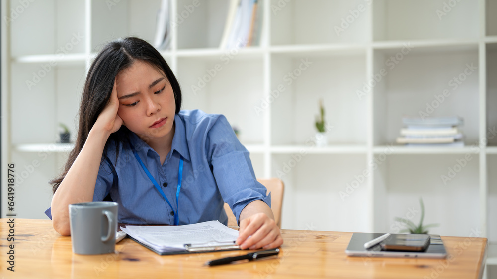 A stressed Asian businesswoman sits at a table and reads a contract with a serious face. A stressed Asian businesswoman sits at a table and reads a contract with a serious face.