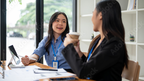 Two happy Asian businesswomen are enjoying talking during a coffee break at a table