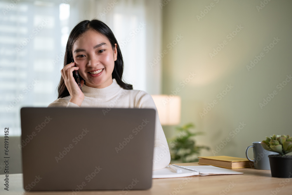 A professional Asian businesswoman is talking on the phone while looking at details on her laptop A professional Asian businesswoman is talking on the phone while looking at details on her laptop