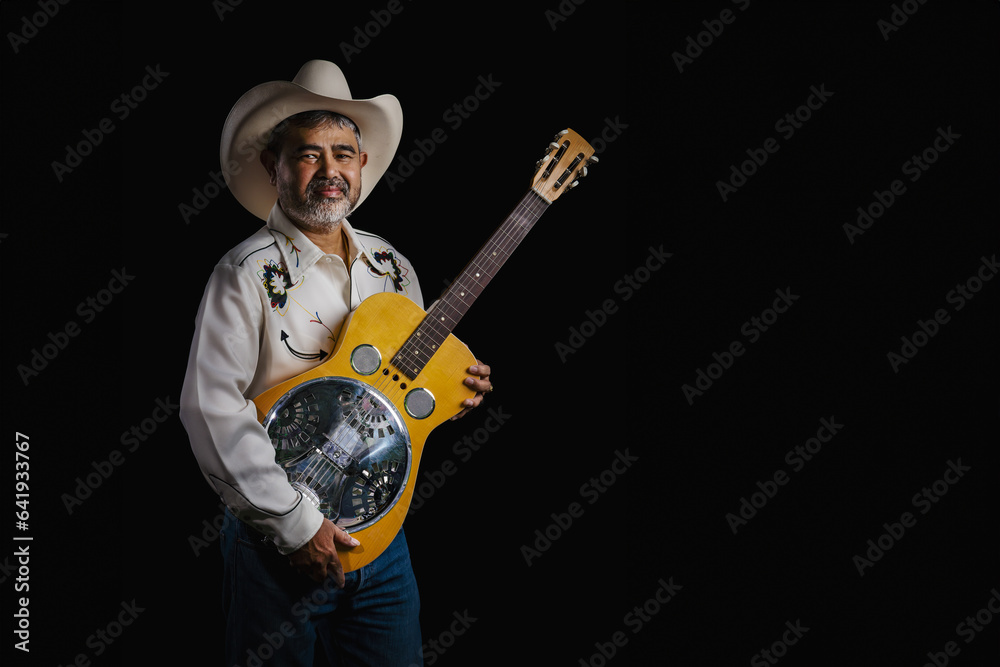 Portrait of bearded Asian musician dons cowboy attire, clutching a Dobro guitar on a black backdrop Portrait of bearded Asian musician dons cowboy attire, clutching a Dobro guitar on a black backdrop