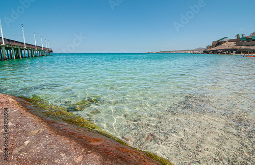 view of the pier in El Coromuel beach, on a beautiful and sunny summer morning with clear blue sky and the transparent sea of ​​Cortes. La Paz Baja, seascape of Mexico