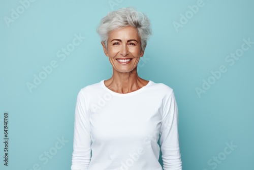 Close up of a 50s middle age woman smiling and wearing a white t-shirt on a turquoise background. Healthy face skin care beauty, skincare cosmetics, dental.