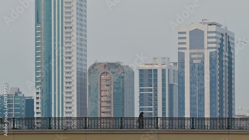 4k: People crossing the bridge, city traffic and modern residential towers in the background, Sharjah, UAE photo