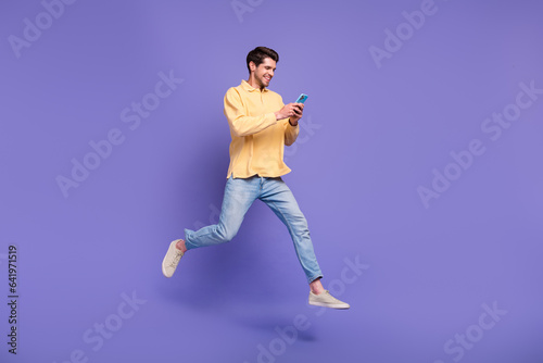 Full length size body photo of jumping funky guy browsing new modern smartphone social media marketer isolated on violet color background photo