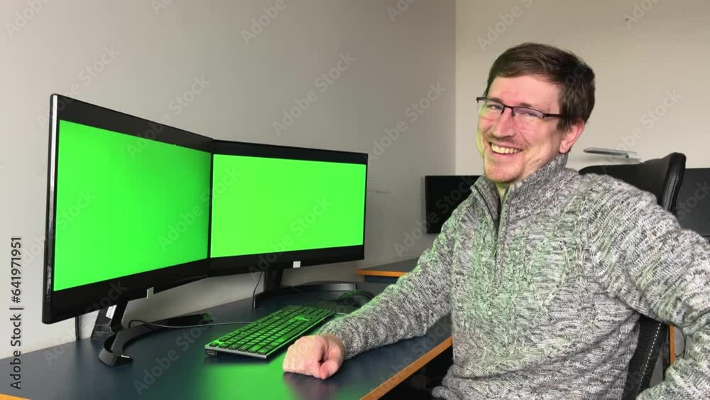 Young 30s businessman in plaid shirt working at table sitting in front of two monitors with green chroma key screen close-up 4k. Young 30s businessman in plaid shirt working at table sitting in front of two monitors with green chroma key screen close-up 4k.