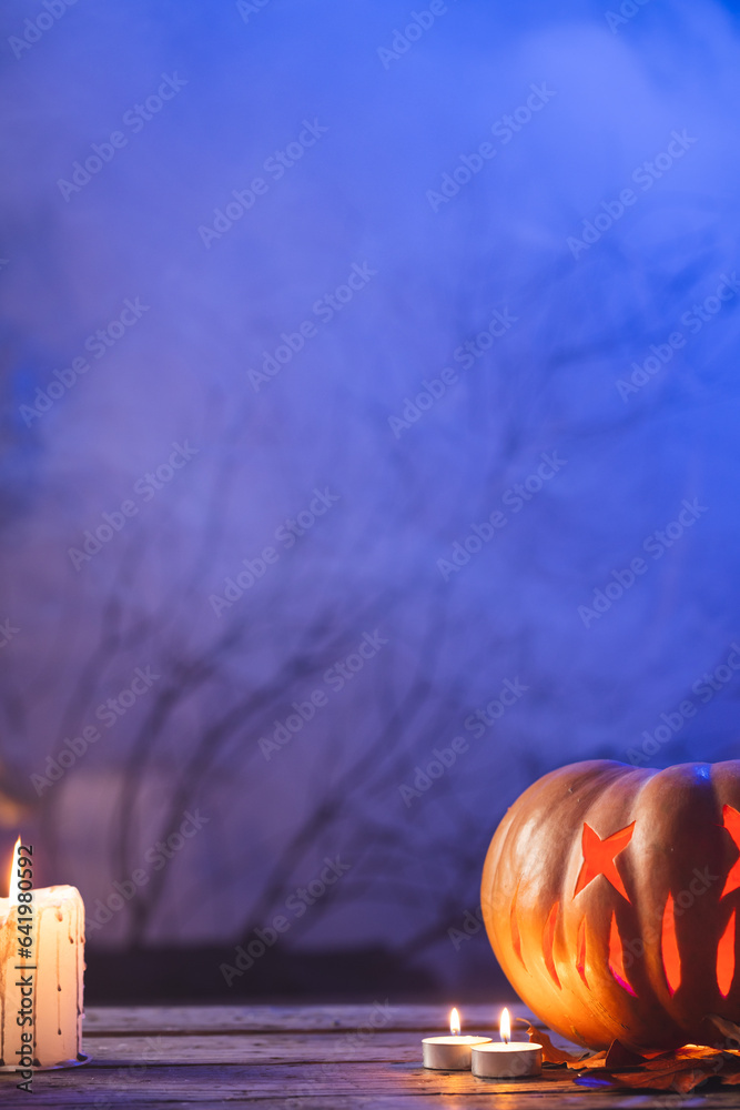 Fototapeta premium Vertical image of carved pumpkin and candle with copy space on blue background